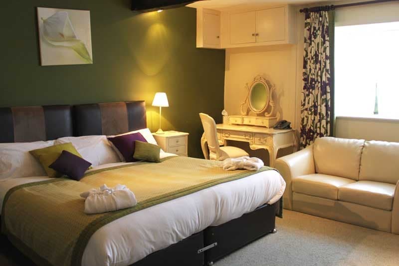 Cozy room with a large bed, green accent wall, elegant vanity, and soft lighting creating a warm atmosphere.