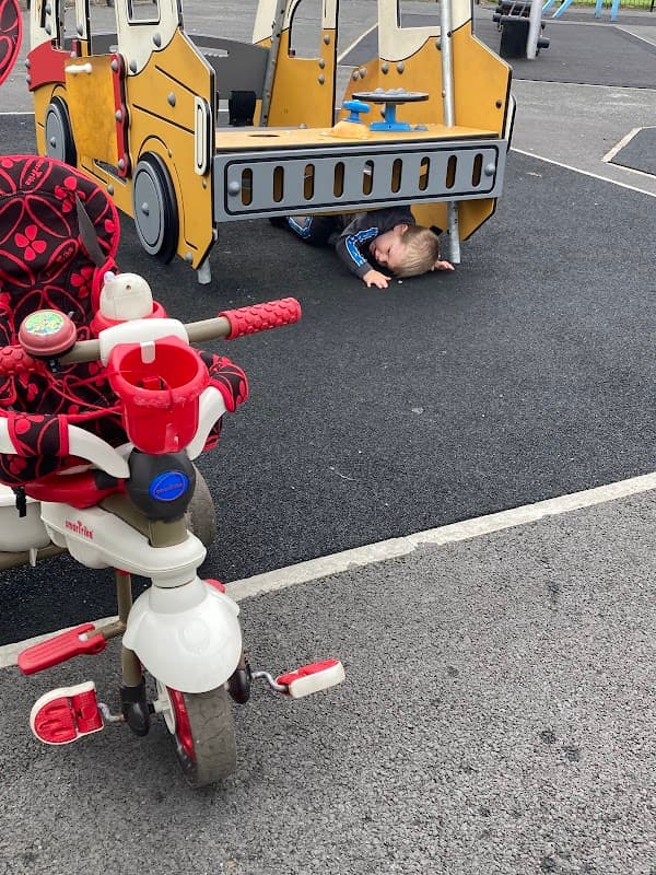 A playground scene with a red tricycle in the foreground and a child crawling under a colorful play structure.