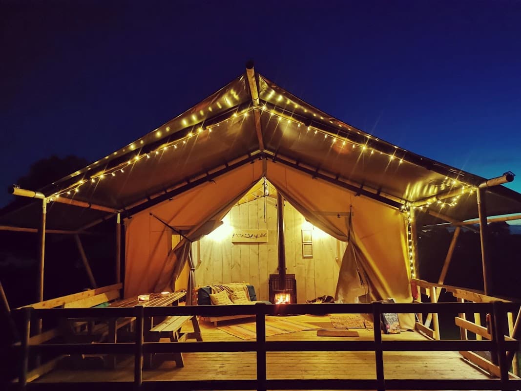 Cozy glamping tent illuminated with fairy lights, wooden deck, and peaceful evening sky at Kingfisher Lakes, Yorkshire.