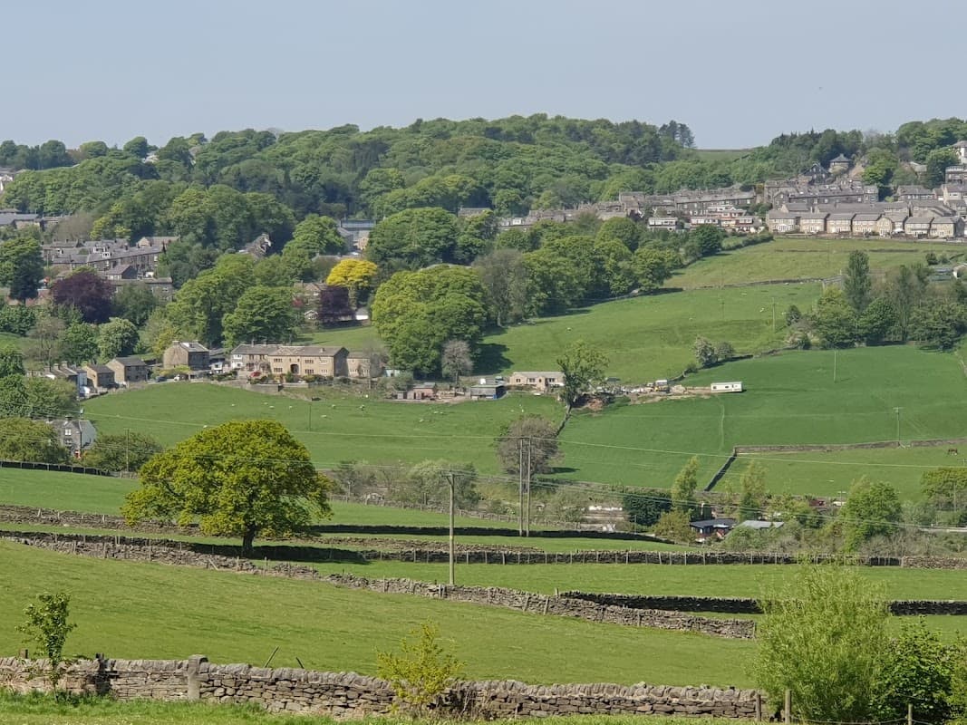 Lush green hills and fields surround Cross Roads Park, with quaint stone buildings and trees dotting the landscape.