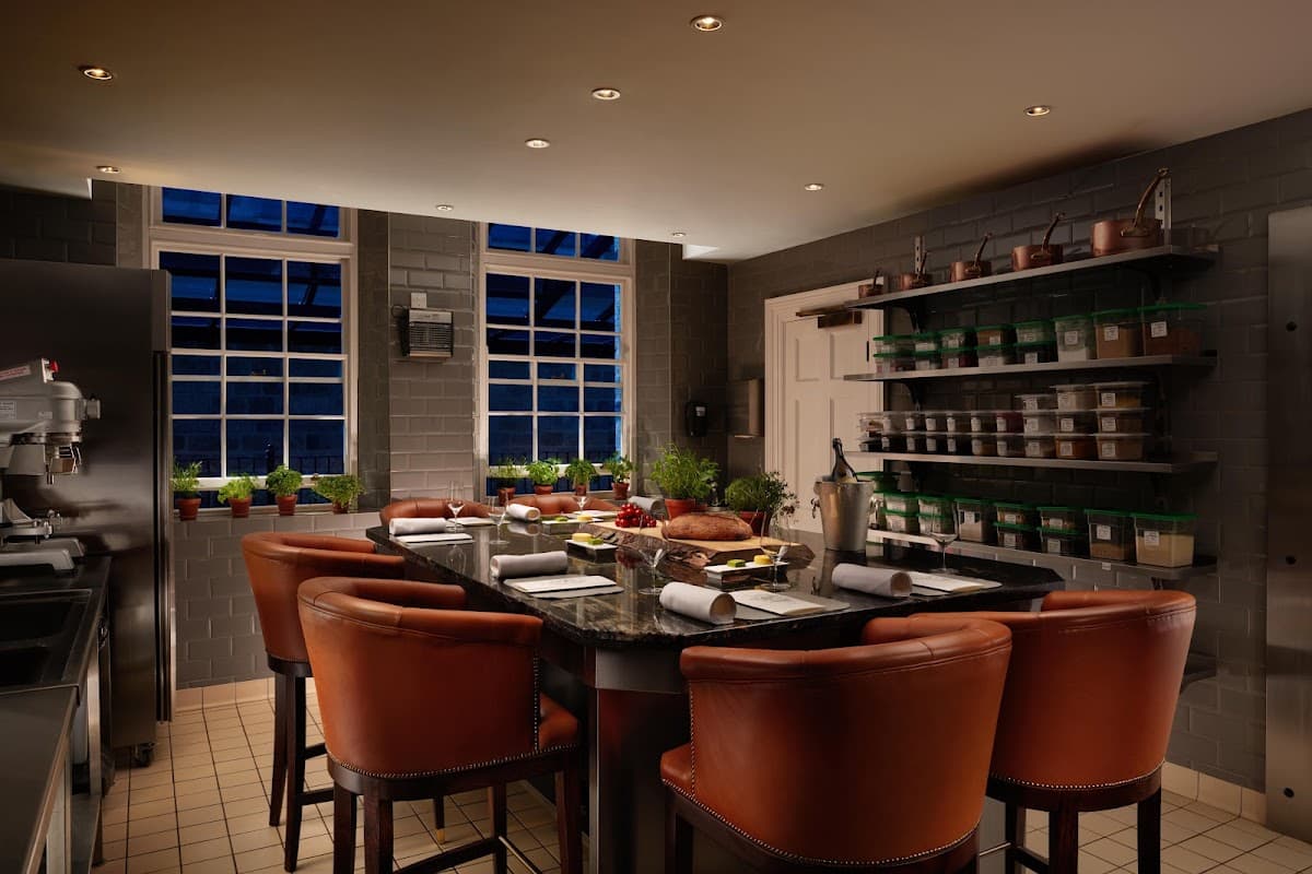 Modern kitchen with dark countertops, leather chairs, large windows, and shelves filled with jars and potted herbs.