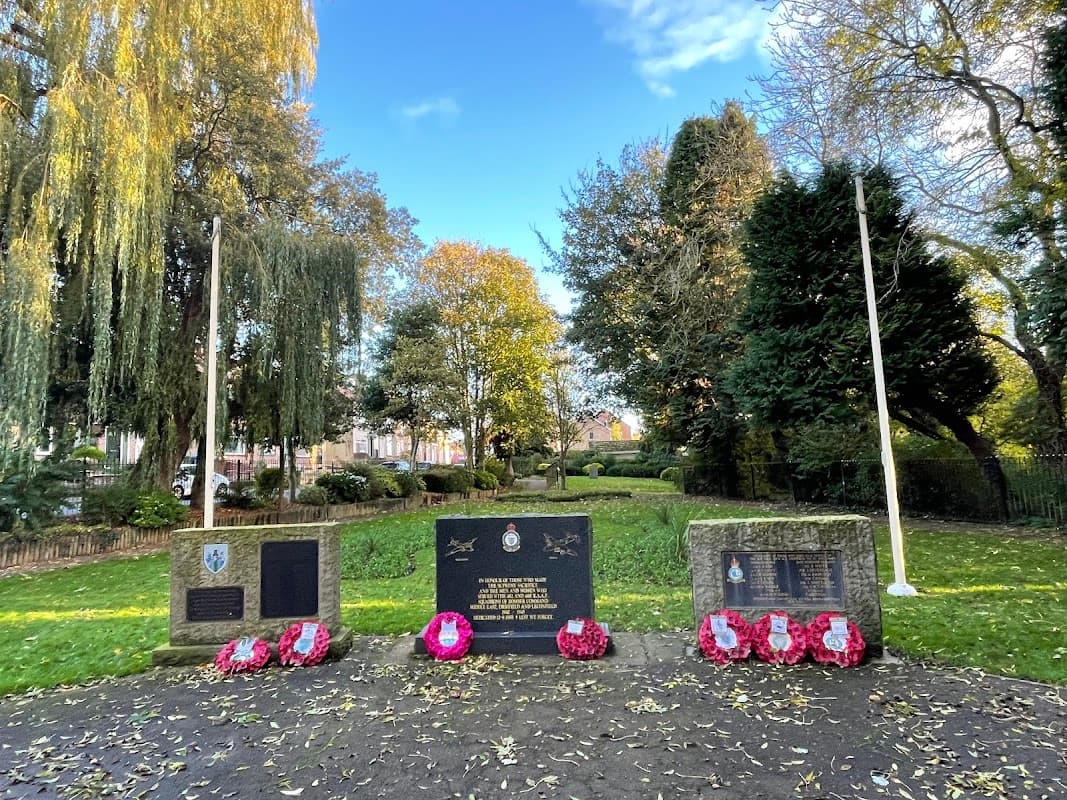 Memorial stones surrounded by trees and greenery, adorned with wreaths in a peaceful park setting.