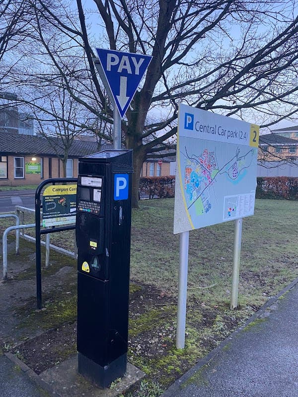 Pay & Display parking meter beside a sign for Central Car Park, with a map and directional arrow in Heslington, Yorkshire.