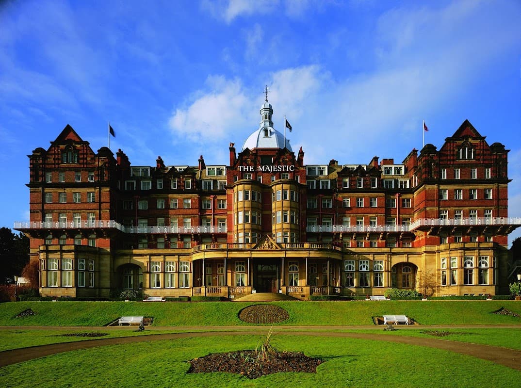 Victorian-style hotel with ornate architecture, large windows, and manicured lawns under a blue sky.