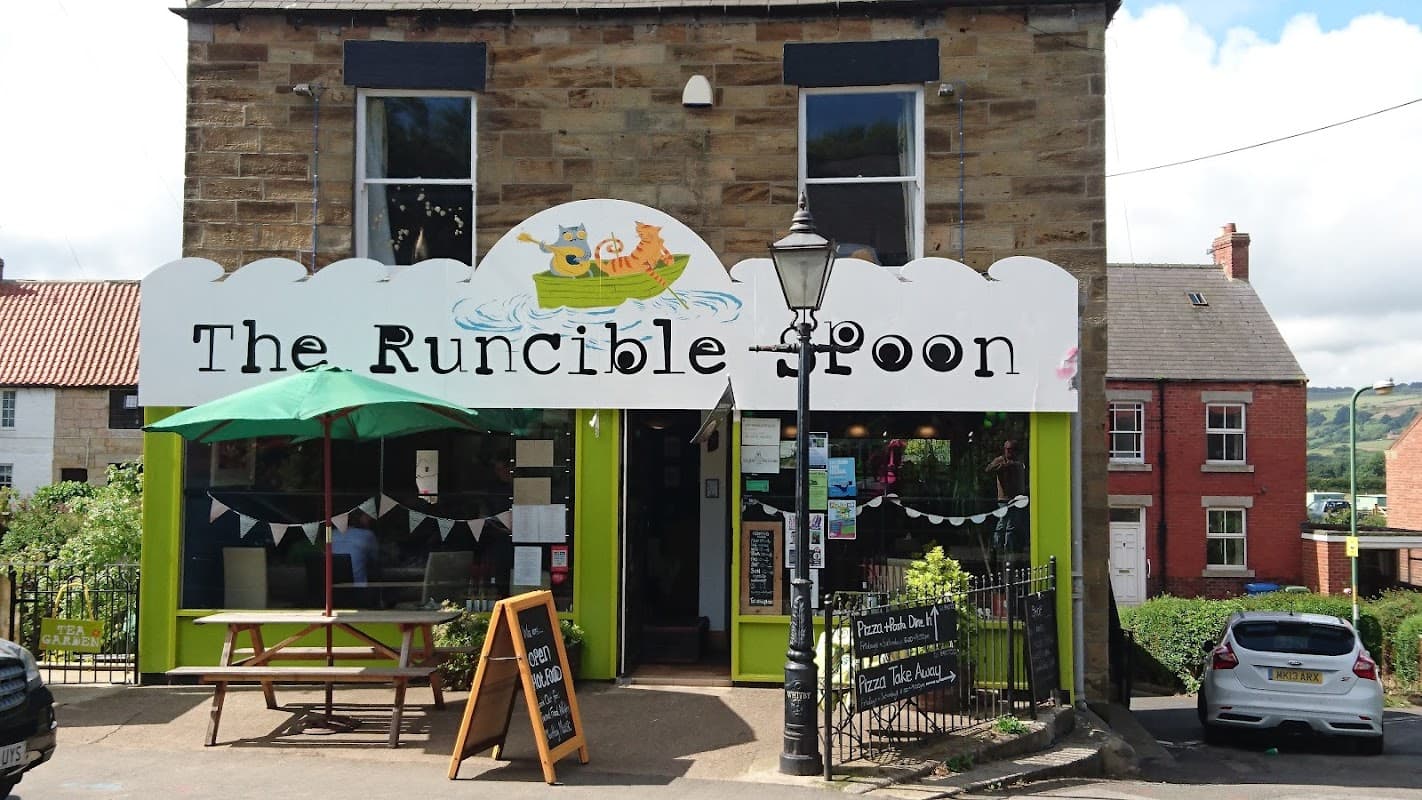 The Runcible Spoon cafΓ© features a colorful sign, outdoor seating, and a green faΓ§ade in Hinderwell, Yorkshire.