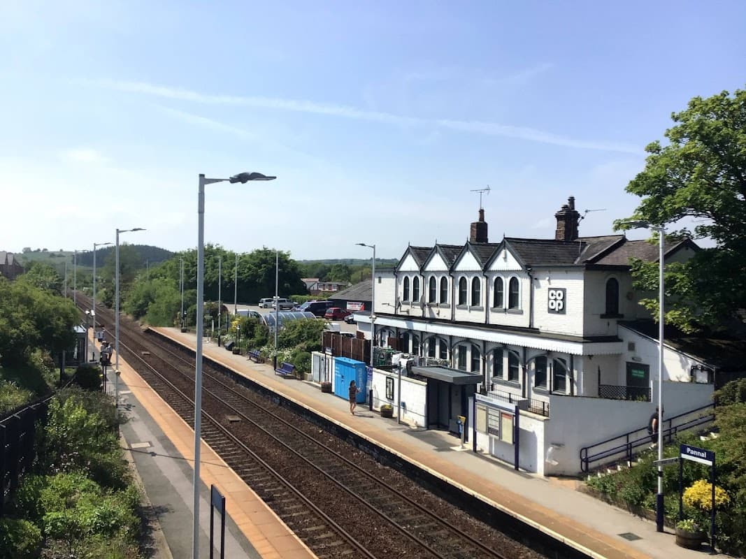 Co-op store and railway station in Pannal, surrounded by greenery and clear blue skies. Train tracks visible.