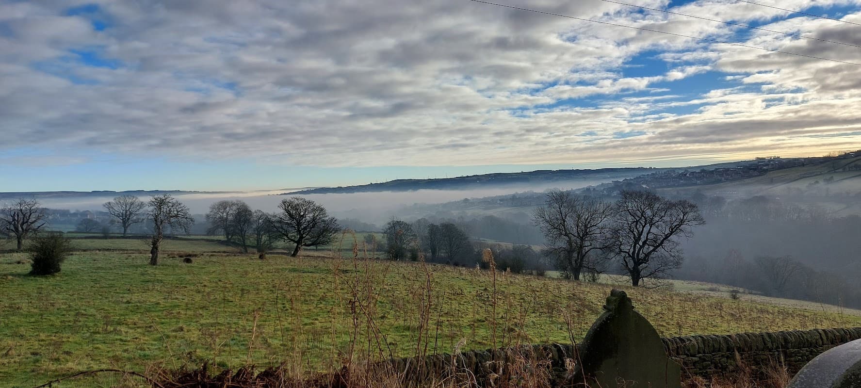 Mist-covered fields with bare trees under a cloudy sky, showcasing the rural landscape of Laycock, Yorkshire.