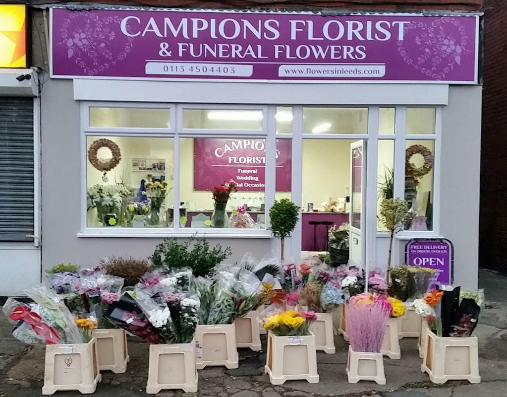 Colorful flower arrangements displayed outside Campions Florist, with a sign indicating open hours and services offered.