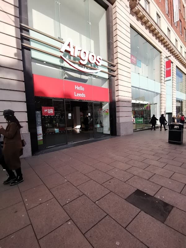 Argos store front in Leeds with a red sign, featuring "Hello Leeds" and shoppers walking by on the pavement.