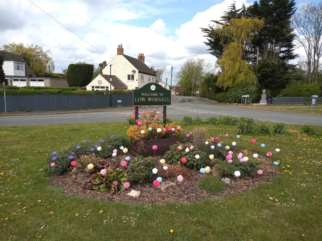 Welcome sign for Low Worsall surrounded by colorful flower beds and greenery on a sunny day.