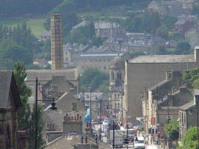 View of Riverside Garage in Luddenden, with surrounding buildings and a hilly landscape in the background.