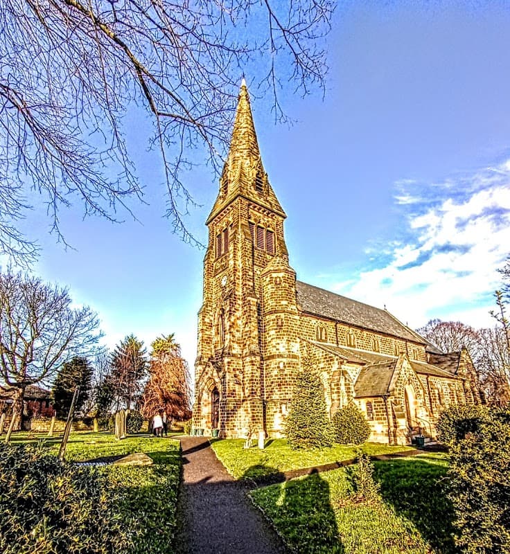 St Paul the Apostle Church with a tall spire, surrounded by trees and a clear blue sky in Monk Bretton, Yorkshire.