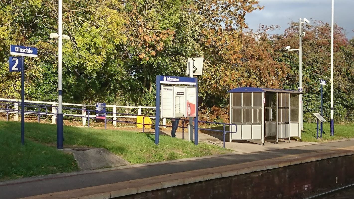Bus stop at Dinsdale station with signage, waiting shelter, and greenery in the background.