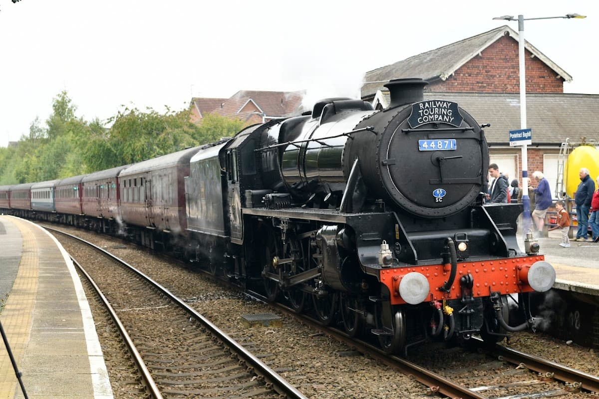 A steam locomotive at Pontefract Baghill station, with vintage carriages and a platform in a rural setting.
