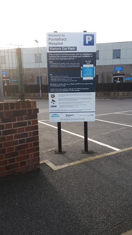Welcome sign for Pontefract Hospital Visitors Car Park with parking rules and information, surrounded by empty parking spaces.