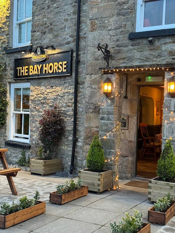 Stone exterior of The Bay Horse pub with warm lighting, wooden seating, and planters outside the entrance.
