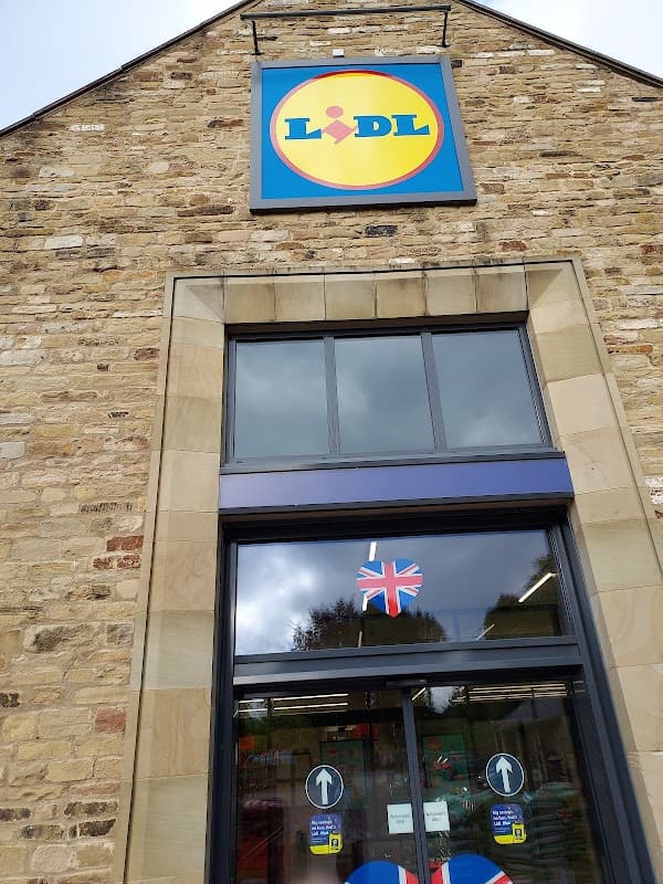 Lidl store facade with a blue and yellow logo, large windows, and a Union Jack flag hanging at the entrance.