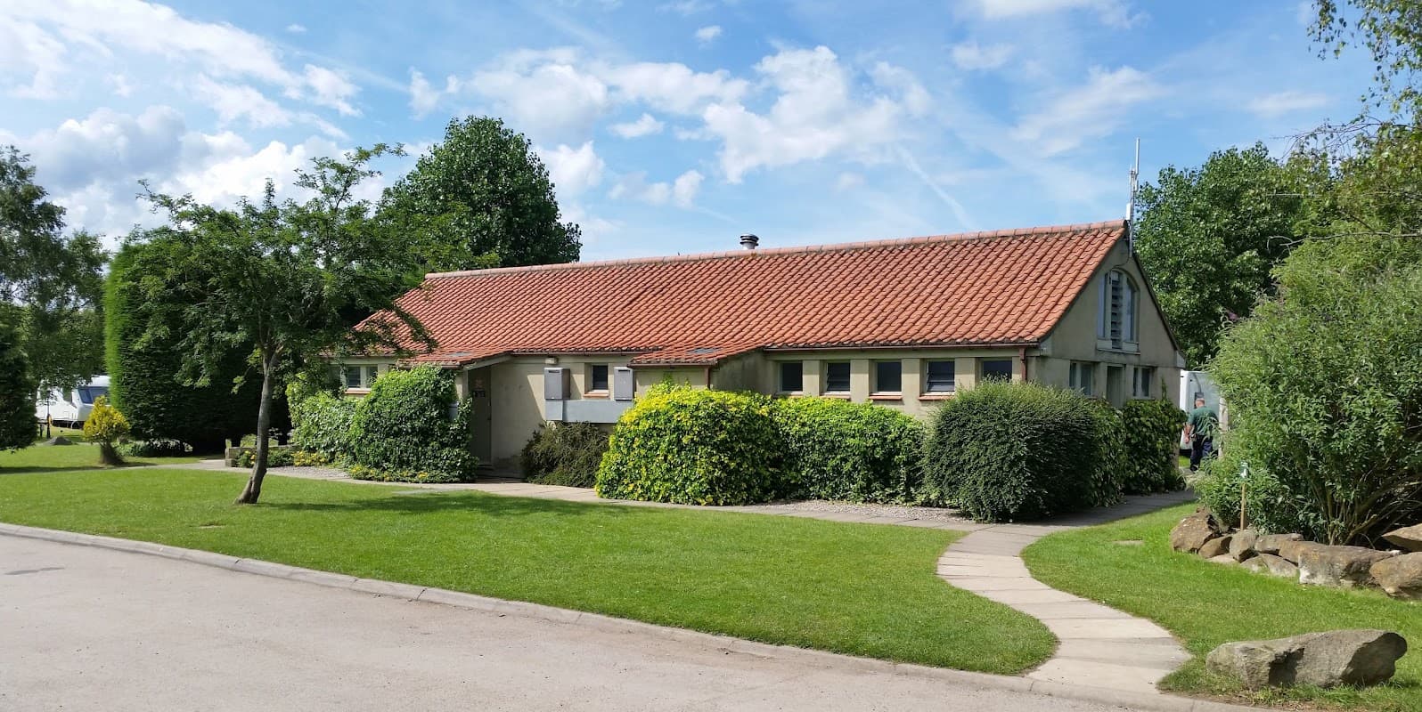 Single-story building with a red-tiled roof, surrounded by greenery and a pathway in Ripley Caravan Park.