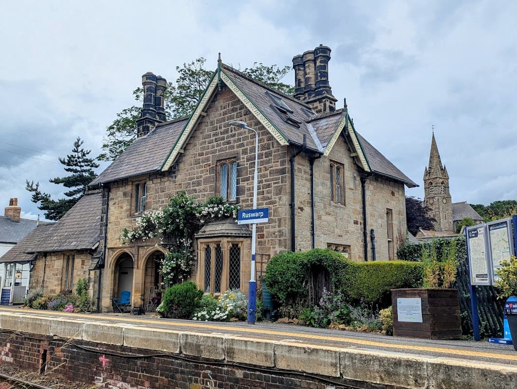 Historic stone building with a slate roof, surrounded by greenery, located at the Ruswarp train station.