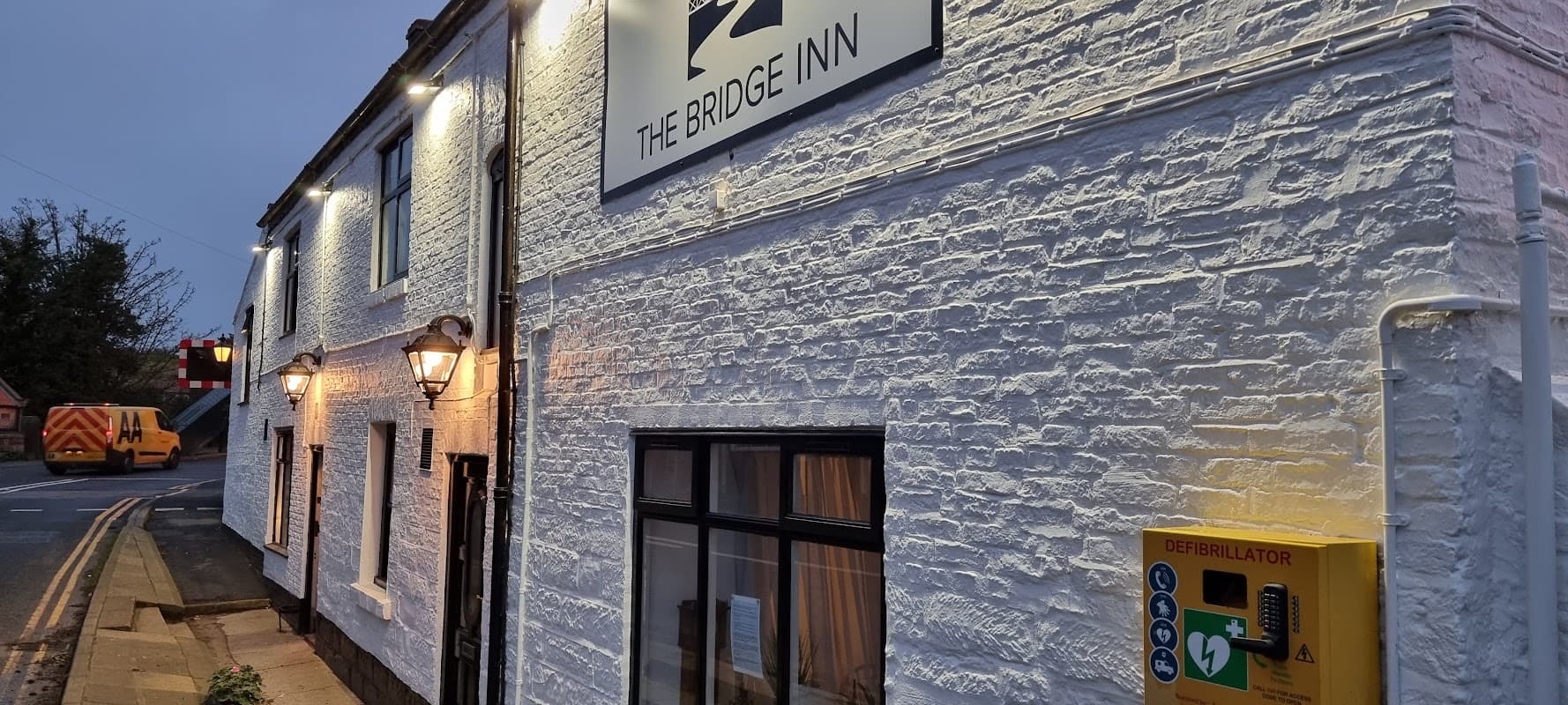 The Bridge Inn bar with whitewashed walls, lanterns, and a defibrillator box outside, set in Ruswarp, Yorkshire.
