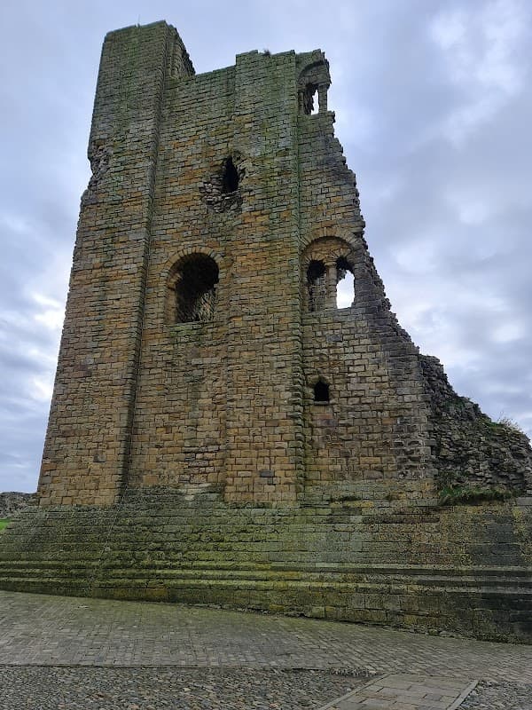 Ruined stone tower with arched openings, set against a cloudy sky, surrounded by grassy terrain.