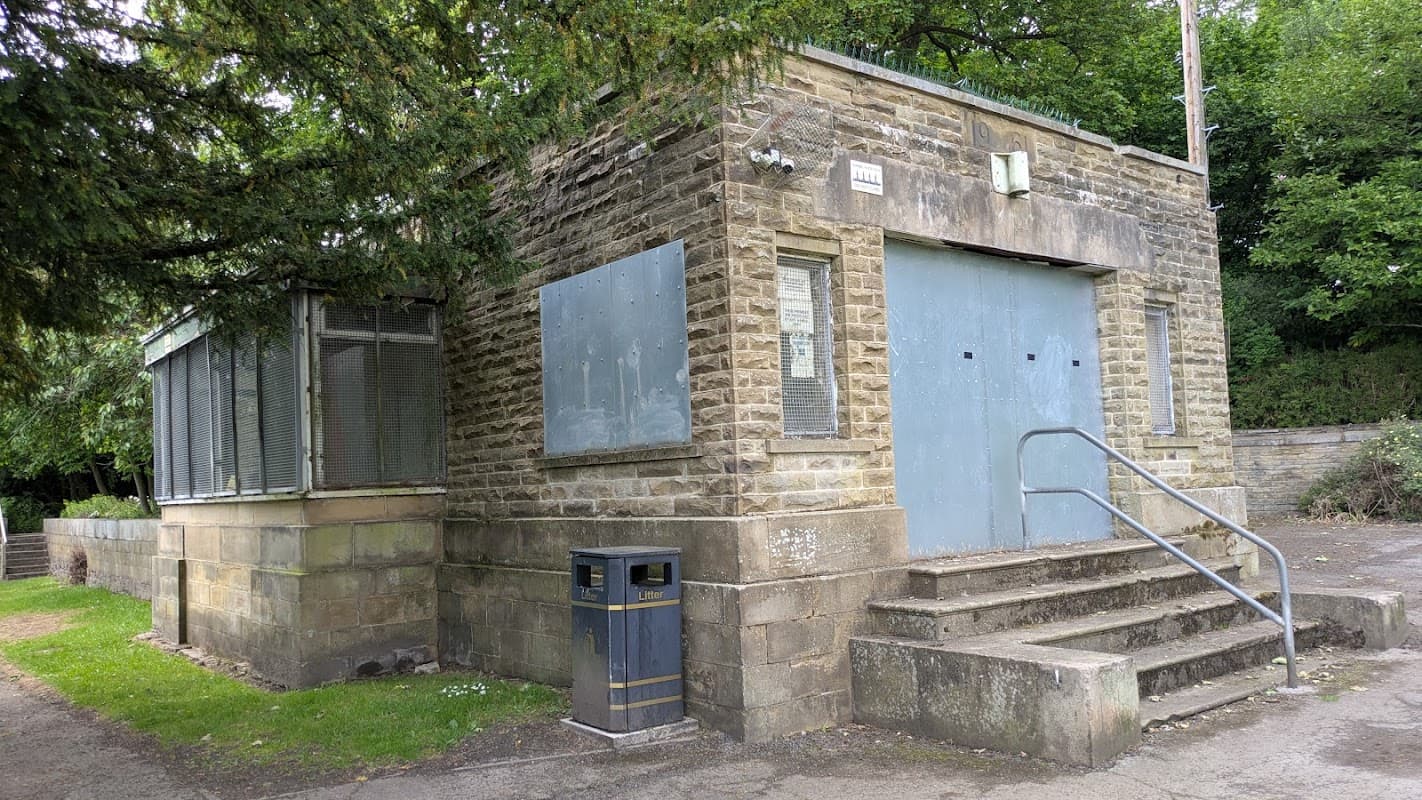 Stone building with a gray entrance, metal railings, and large windows, surrounded by greenery in Shelf, Yorkshire.