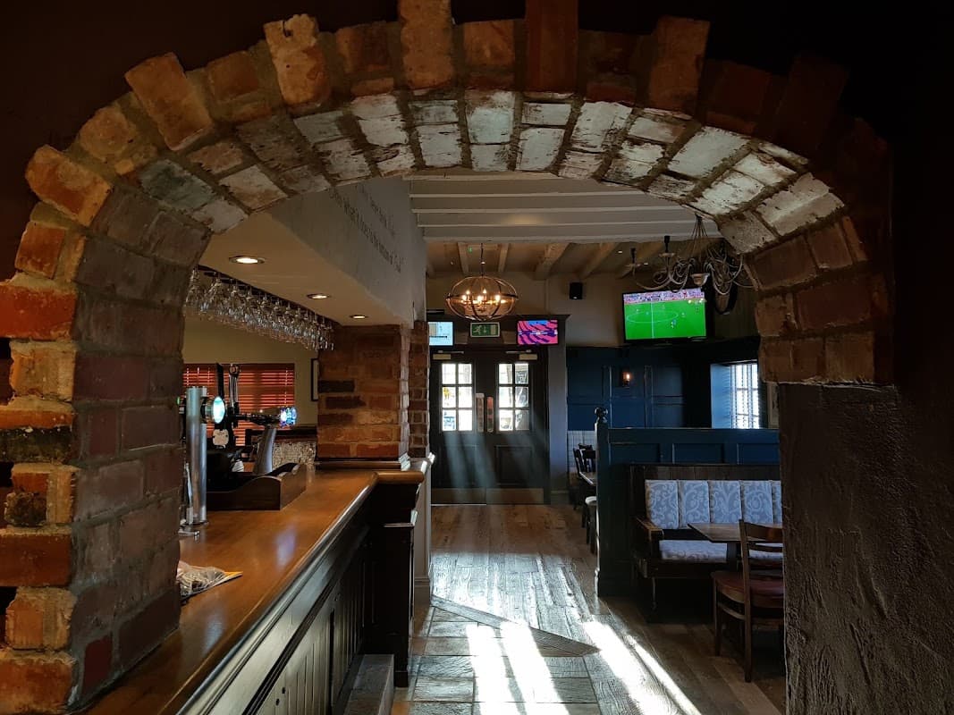 Brick archway leading to a cozy pub interior with wooden floors, bar, and TVs showing sports.