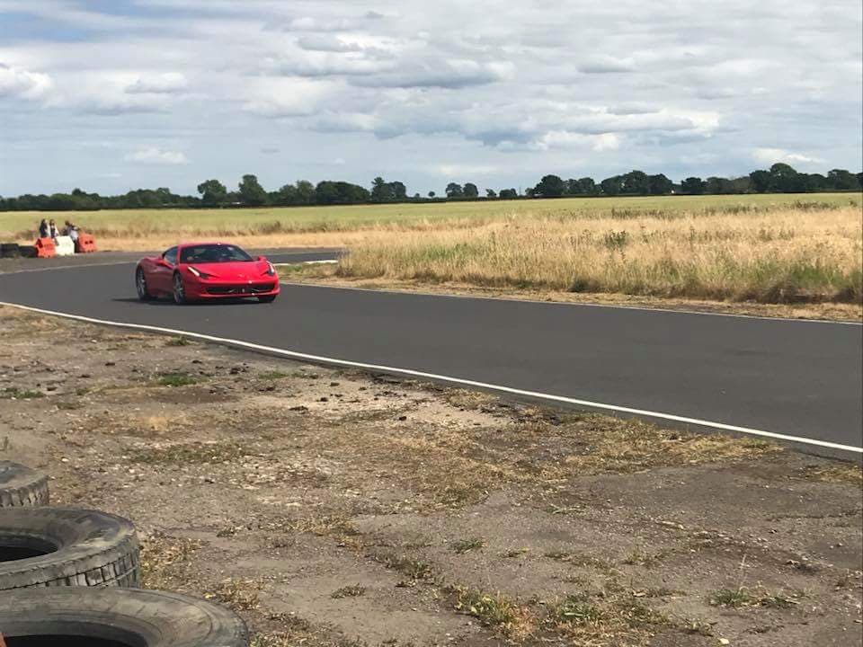 Red sports car on a racetrack surrounded by open fields and cloudy skies at Tockwith Motor Sports Centre.