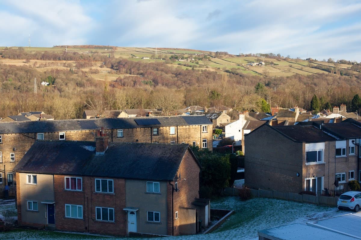 Dalesgate Hotel surrounded by residential buildings and rolling hills under a partly cloudy sky in Utley, Yorkshire.