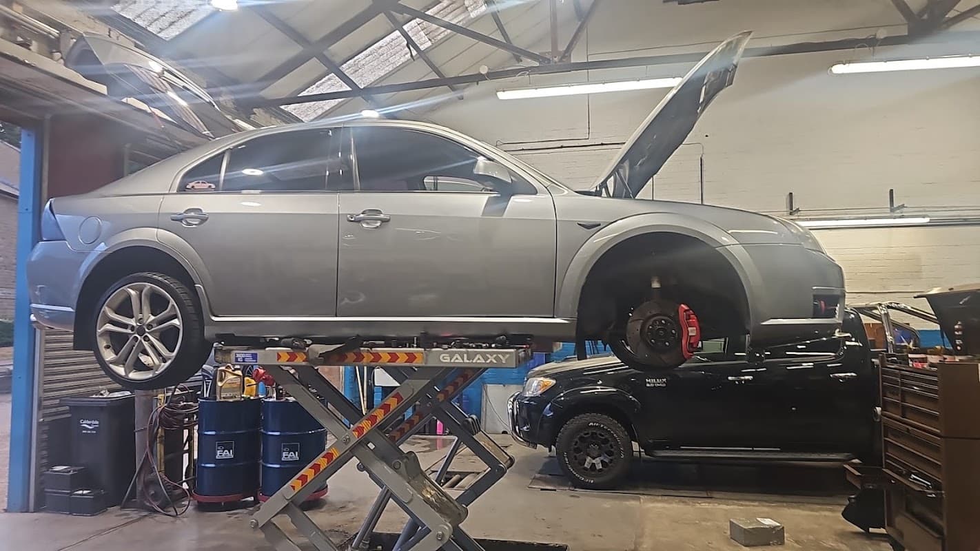 A silver car on a lift in a garage, with tools and equipment visible in the background.
