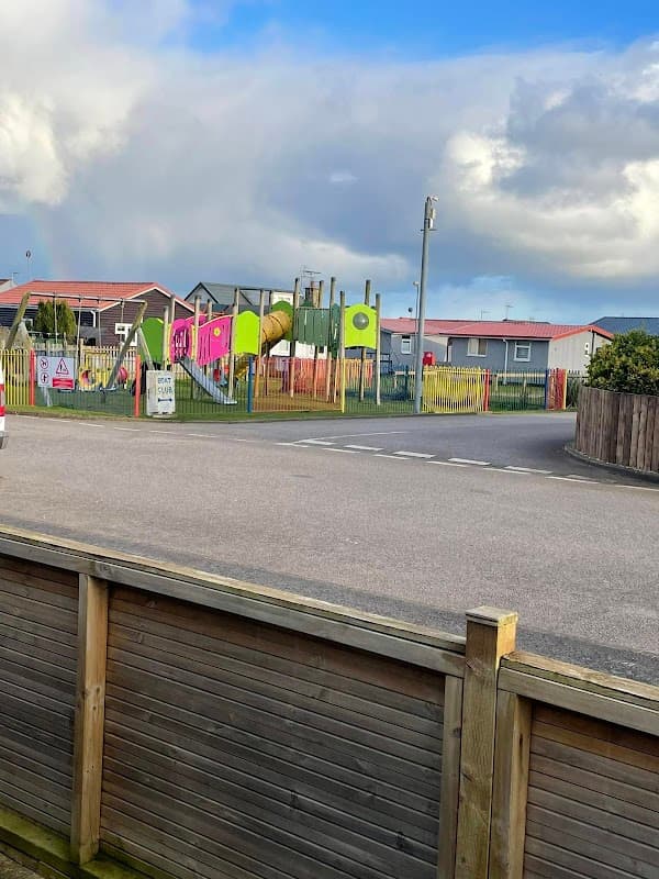 Colorful playground with slides and climbing structures, surrounded by holiday park accommodations under a cloudy sky.