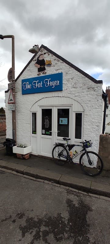 Quaint white building with blue sign "The Fat Fryer", bicycle parked outside, and decorative elements on the facade.
