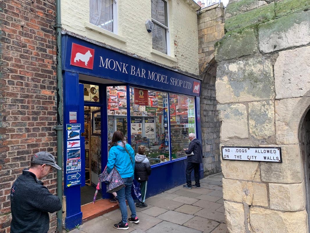 Colorful storefront of Monk Bar Model Shop with people browsing, surrounded by historic stone walls.