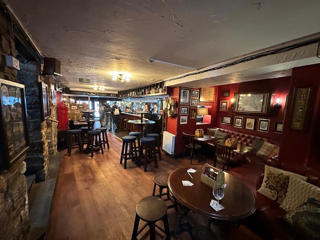 Cozy pub interior with wooden floors, red walls, bar area, framed pictures, and wooden stools around tables.