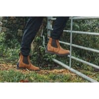 Brown leather Amblers Aldingham Dealer Boot with elastic side panels and rugged sole, worn by person climbing a gate.