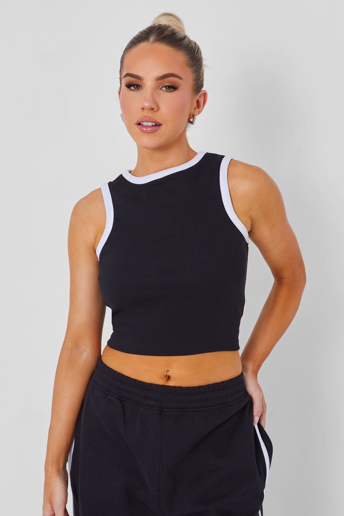Black ribbed vest with white contrast binding along the neckline and armholes, featuring a cropped fit and worn with black sweatpants.