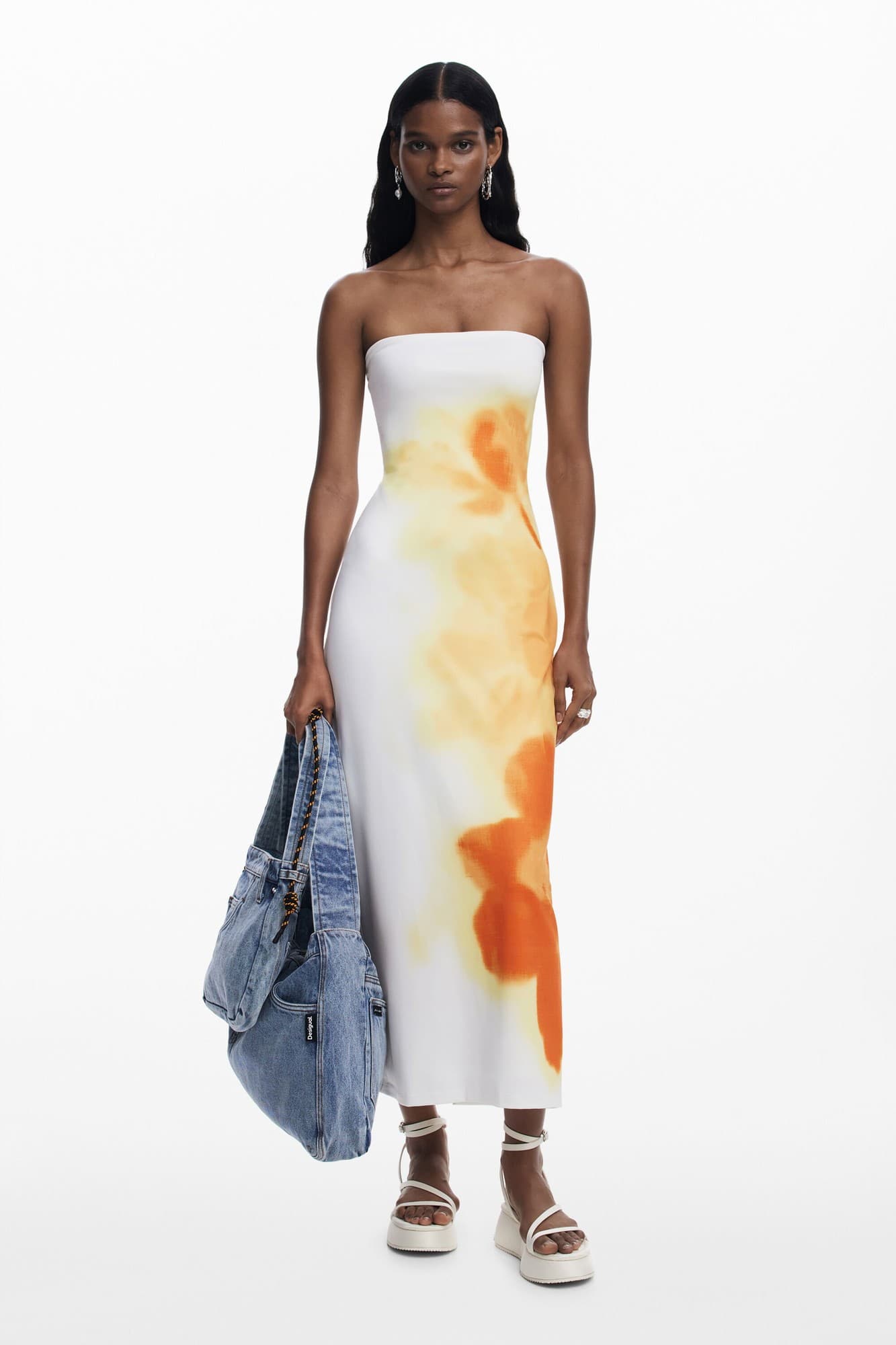 Strapless white dress with orange and yellow watercolor patterns, paired with a denim bag and platform sandals, showcasing a sleek, modern silhouette.