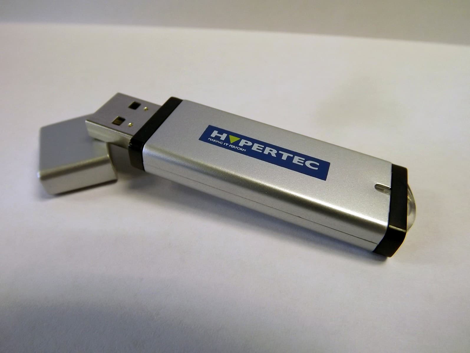 Silver USB drive with a hinged cap, featuring a black band and the "HYPERTEC" logo in blue, labeled as a 64GB EnCryptPLUS HyperDrive with AES-256 encryption.