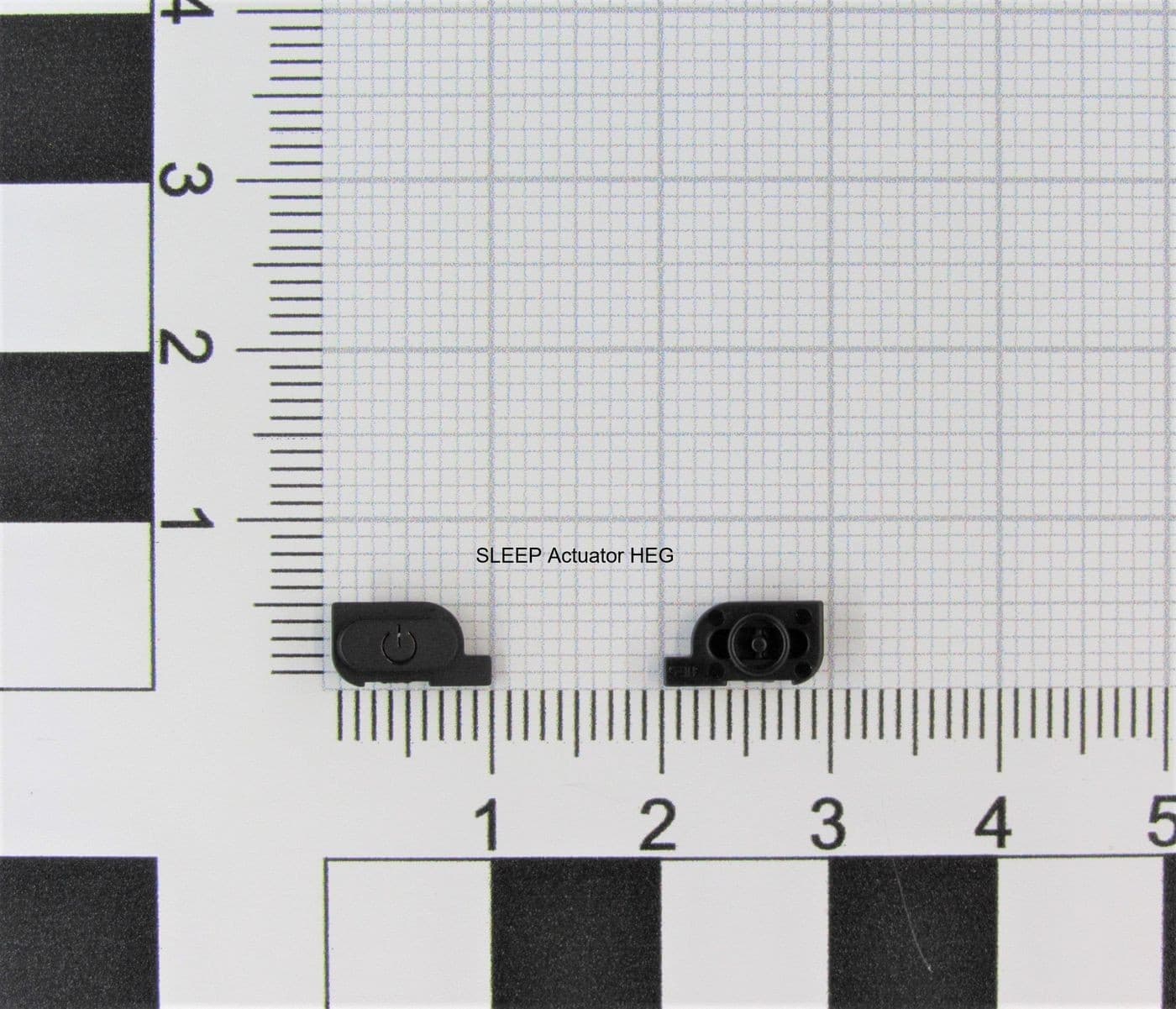 Black Nintendo C/SLEEP(K1) HEG actuator, featuring a compact design with a circular button and a small lens, placed on a grid background for scale.