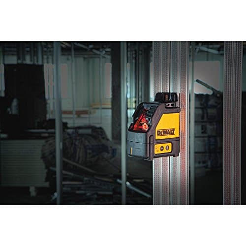Yellow and black DEWALT DW088K-XJ self-leveling cross line laser level mounted on a vertical surface, featuring a red laser line and control buttons for precise alignment.