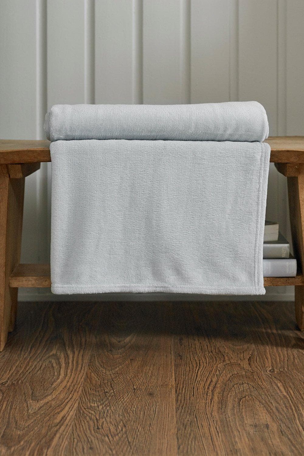 Silver ultra-soft throw blanket by Deyongs, featuring a luxurious snuggle touch, elegantly draped over a wooden bench with books underneath.