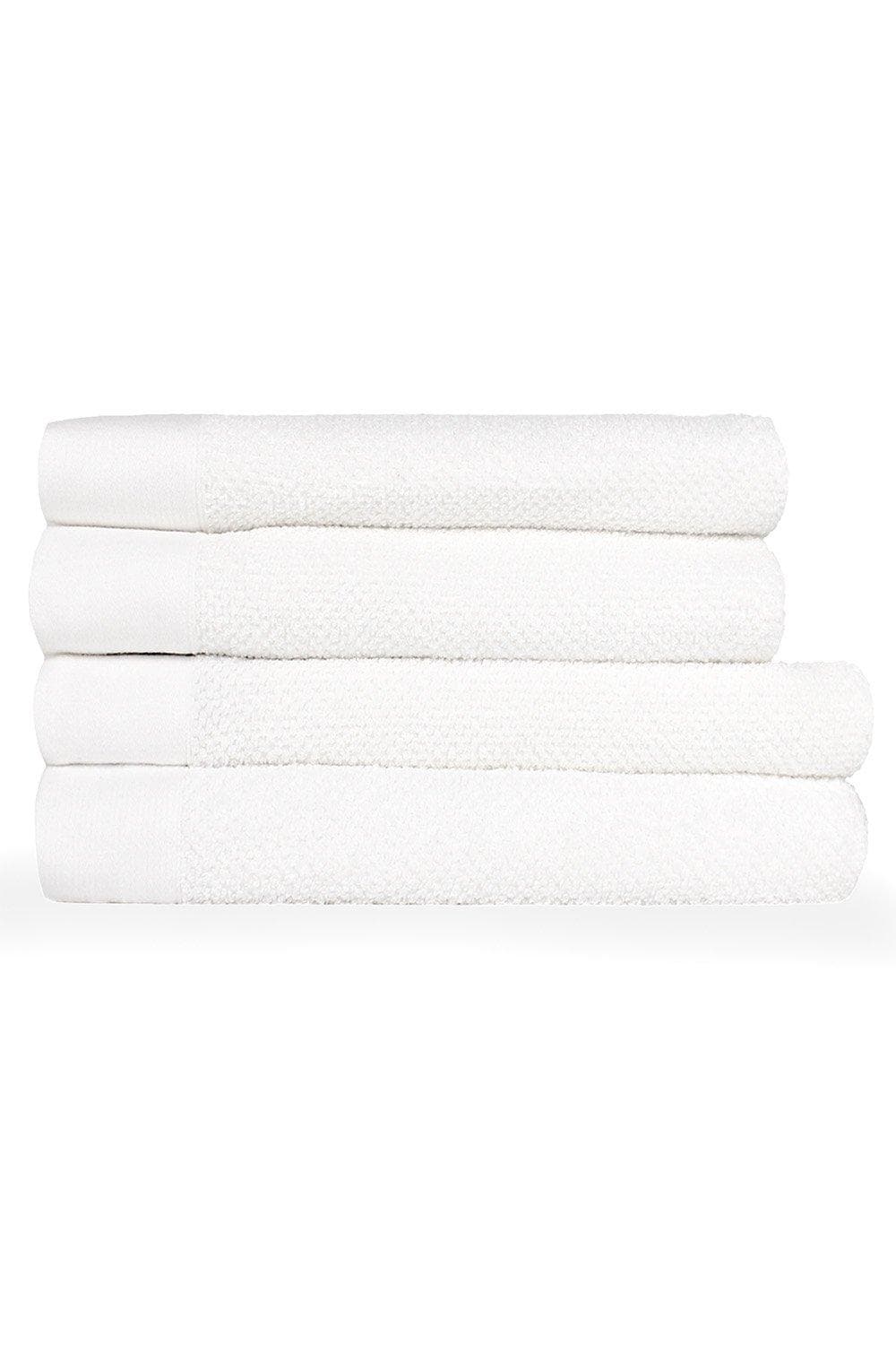 Four neatly stacked white cotton bath towels featuring a textured weave and panel design, ideal for a luxurious bathroom experience.