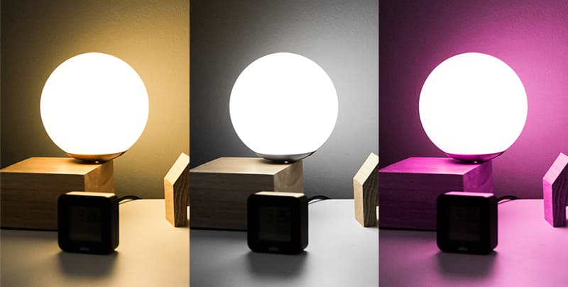LogiLink WiFi Smart E27 R63 Reflector Bulb with a round, white glass exterior, displayed in three color settings: warm yellow, cool white, and vibrant purple, on a wooden base.