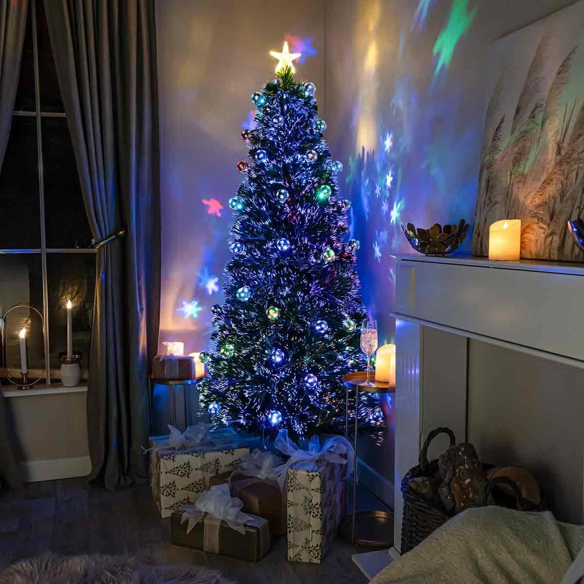 A 4ft green fibre optic Christmas tree adorned with colorful lights and a star topper, surrounded by wrapped gifts and glowing candles in a cozy room.