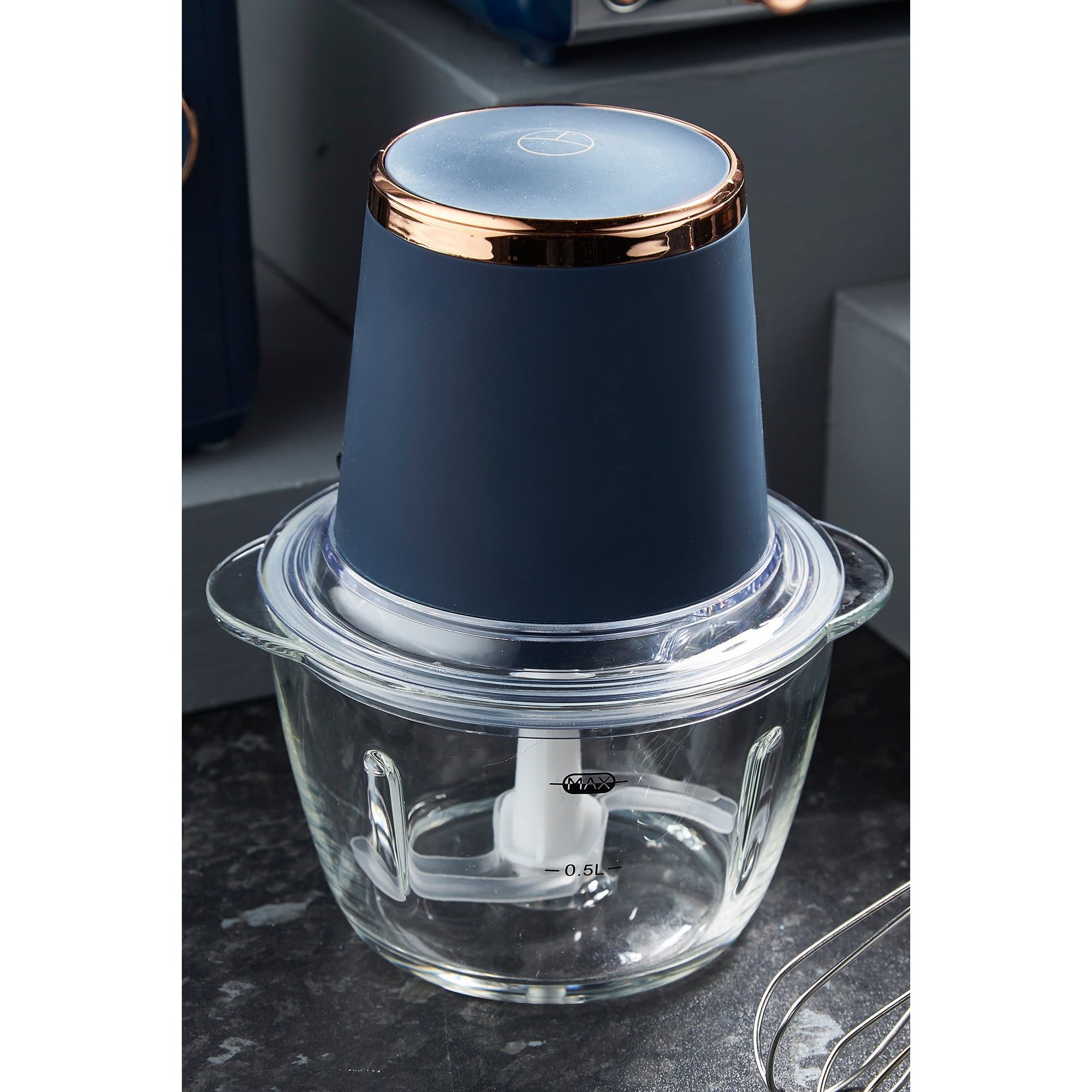 Black mini chopper with a sleek design, featuring a glass bowl, white chopping blade, and a navy blue lid with a rose gold accent.