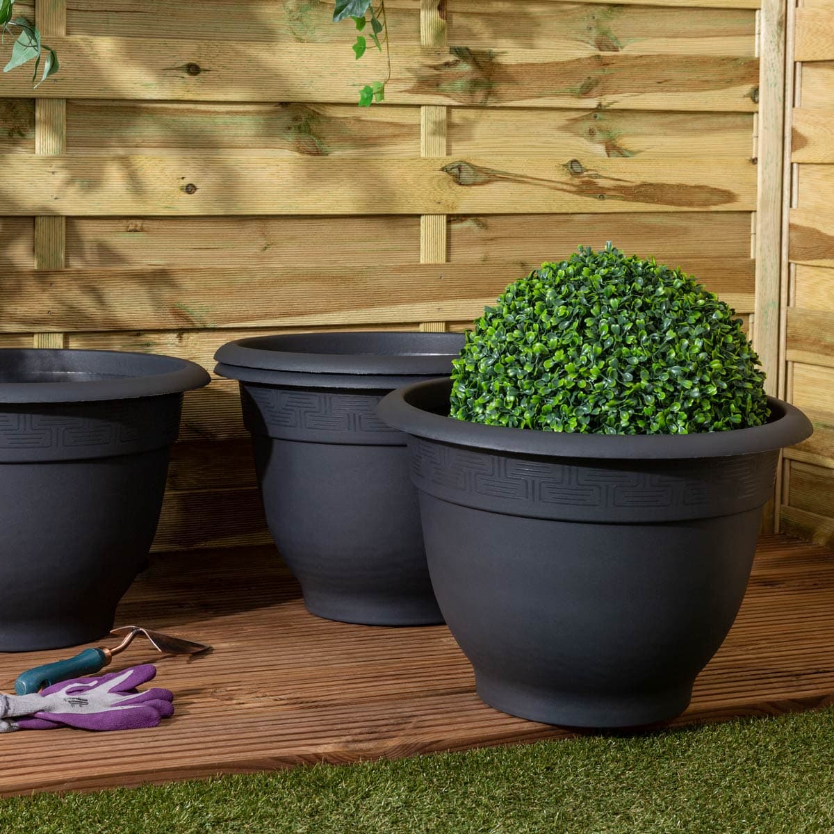Round 48cm planter in slate black, made of durable plastic, featuring a textured design, placed on wooden decking with a faux greenery ball inside.