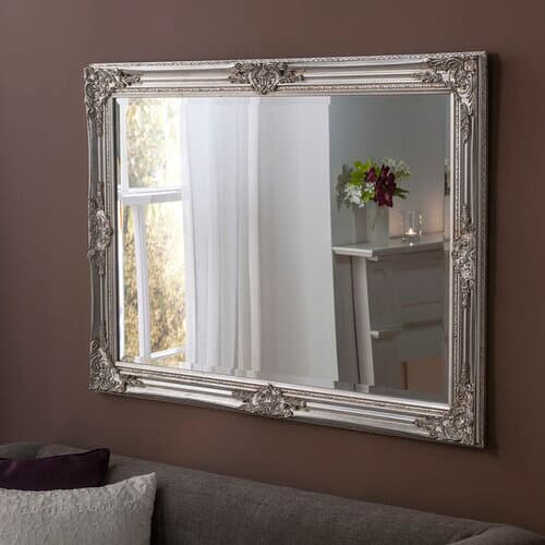 Decorative full-length mirror in metallic silver, featuring an ornate frame with intricate detailing, measuring 74x163cm, reflecting a soft-lit room with a floral arrangement.