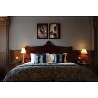 Luxurious hotel room with ornate wooden headboard, plush bedding, decorative pillows, and warm bedside lamps.