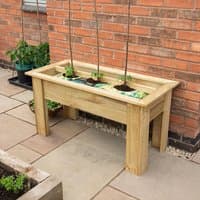 Wooden Forest Grow Bag Planter, rectangular with four sturdy legs, placed on a patio against a brick wall.