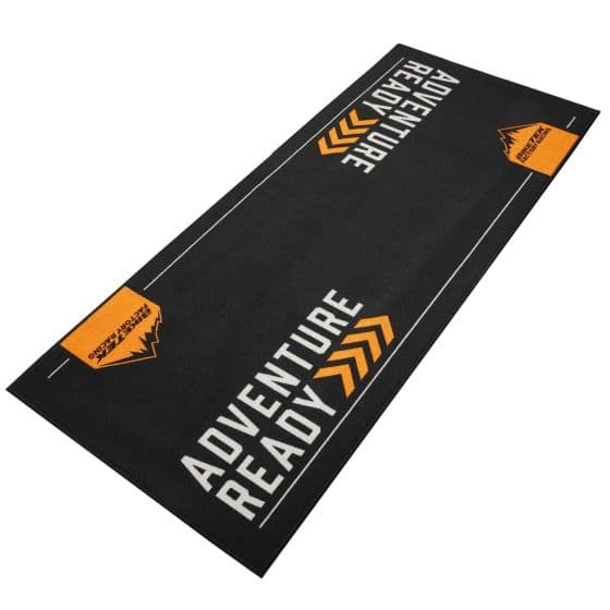 Black carpet with "ADVENTURE READY" in bold orange letters, featuring a mountain graphic and white lines along the edges, designed for outdoor and biking enthusiasts.